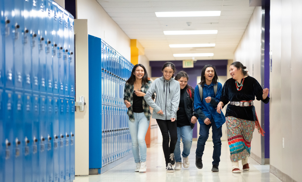 a group of high school students walking in a hallway with blue lockers on the left
